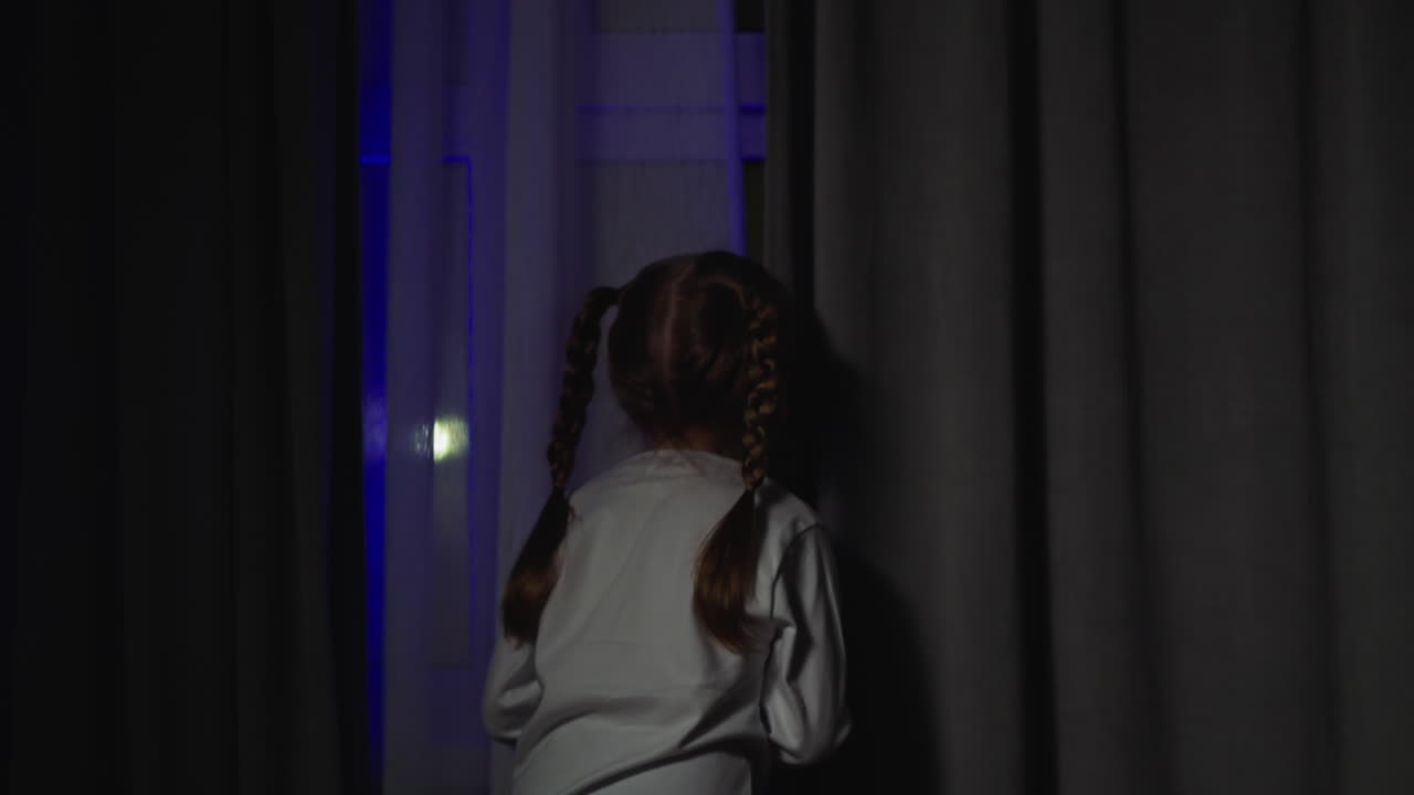 Little girl walks to window enjoy flashing firework lights