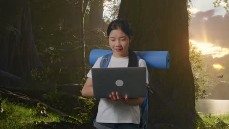 asian female hiker with mountaineering backpack using a laptop while exploring forest nature