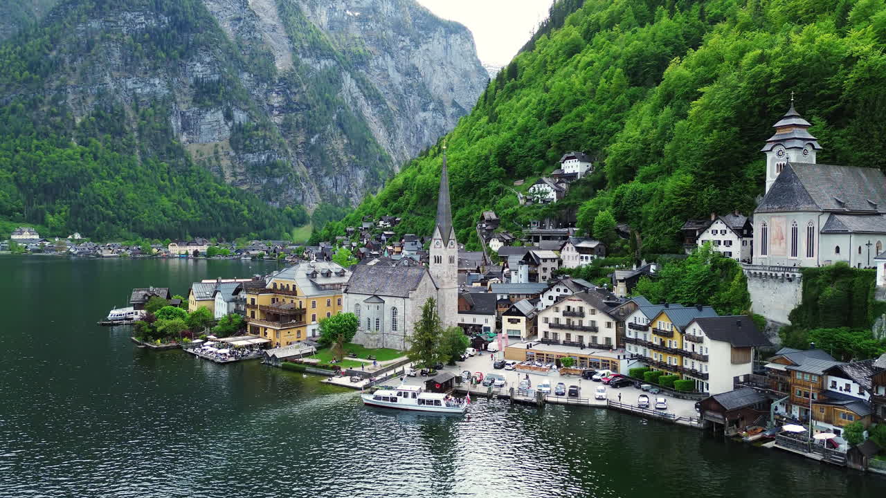 Ferry Boat At The Terminal With Hallstatt Town Church And Lakefront Houses In Austria. - aerial shot
