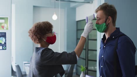 African-american-woman-wearing-face-mask-measuring-of-her-male-colleague-at-modern-office