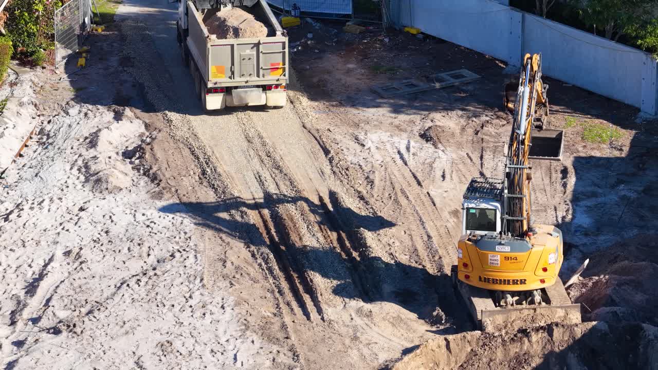 Aerial drone footage of excavator and dump truck moving dirt at sunny construction site