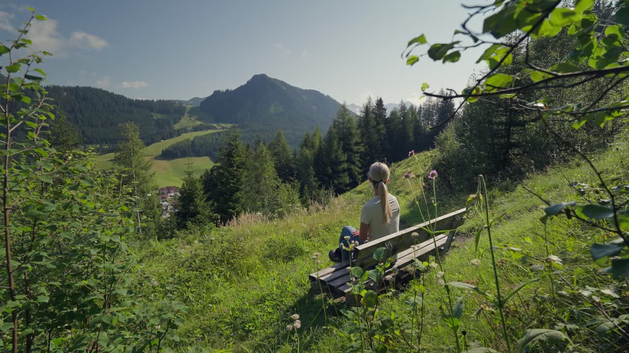 Woman sits on a bench admiring mountain views and lush nature in Berwang, Austria