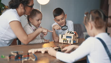 female teacher helps little boy and girls interested in science and technology to build robots