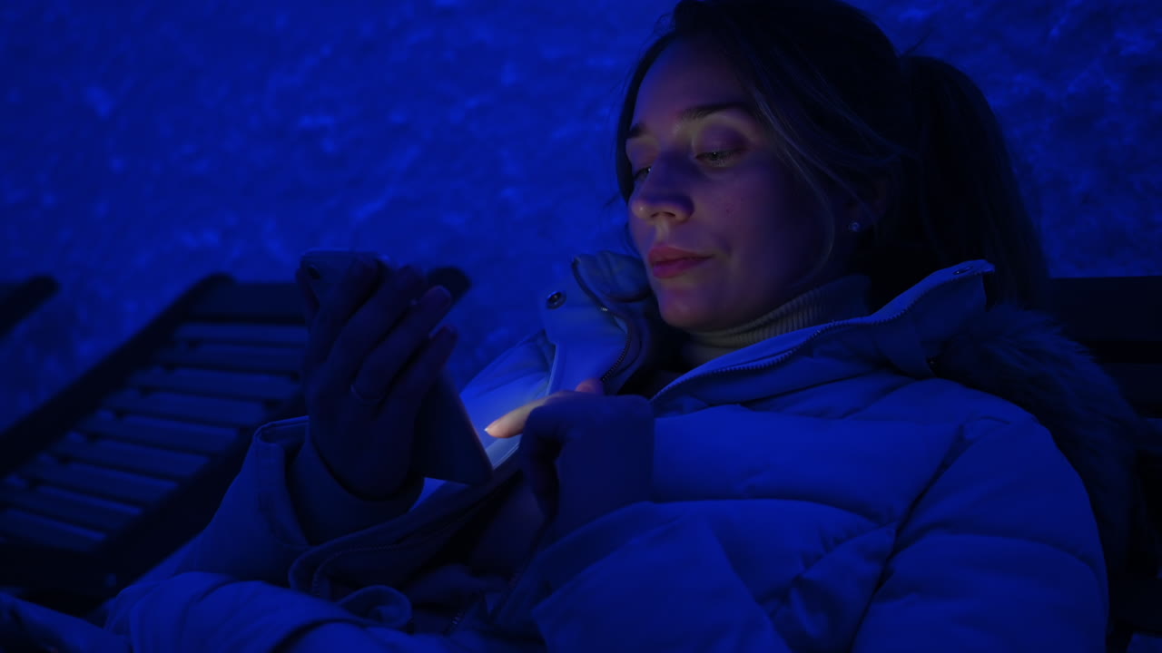 Donna che si rilassa su una sedia di legno in una stanza di sale con luce blu, mentre lavora al cellulare