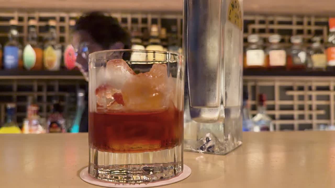 Primo piano di un cocktail rosso in un bicchiere tumbler su un bancone da bar in legno.