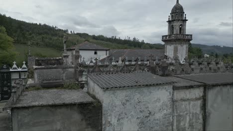 Aerial-rising-of-cemetery-and-church-of-San-Xurxo-de-Moeche-on-cloudy-day,-Spain