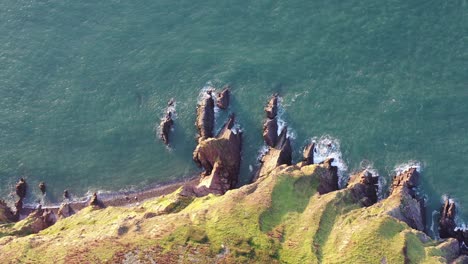 Drone-shot-looking-down-on-a-rocky-coastal-scene,-with-ocean-waves-crashing-into-rocks-on-the-North-Devon-coast-,-UK