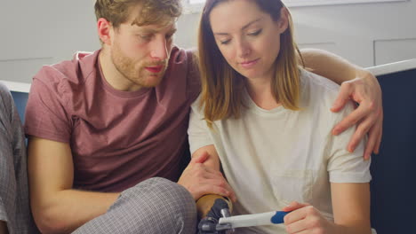 disappointed couple with woman with prosthetic arm sitting in bathroom with negative pregnancy test