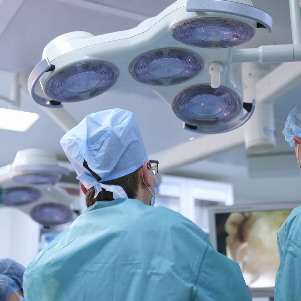 Surgery in modern clinic. Rear view of doctors in medical uniform performing an operation and looking on the monitor. Group of surgeons in the operating theatre