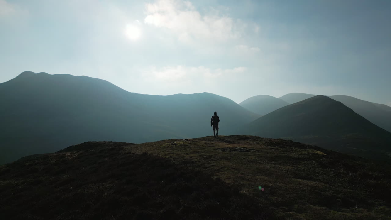volando más allá de la silueta del excursionista en la cumbre de la montaña hacia las montañas nubladas en el distrito inglés del lago uk
