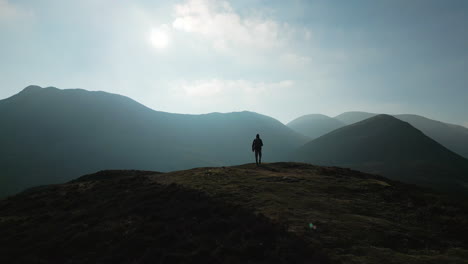 flying past hiker silhouette on mountain summit towards misty mountains in english lake district uk