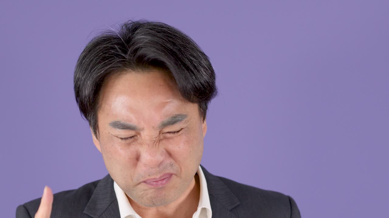 紫色の背景の前で、スーツを着た中年ビジネスマンが驚いた表情で、身振り手振りで力強く反応している。