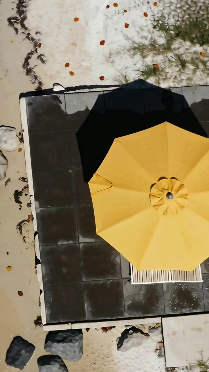 Video verticale: Drone che riprende con panoramica un patio piastrellato sulla spiaggia, rivelando un ombrellone giallo e una sedia a sdraio.