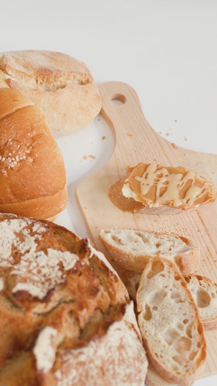 Overhead camera pans across sourdough, baguettes, and croissants with peanut butter on a board.