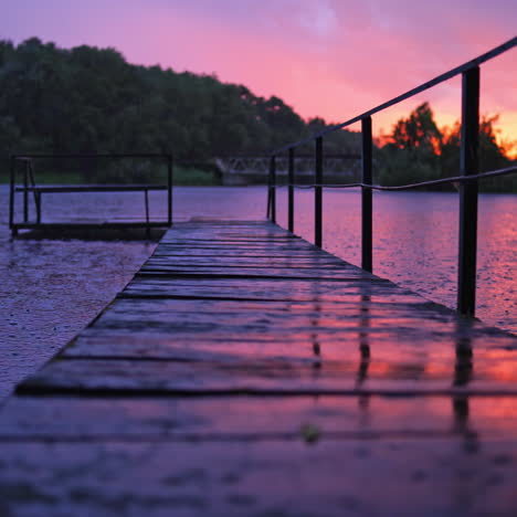amazing view of rain falling on the water and footbridge at sunset. wet wooden bridge over the lake with nobody in the evening in rural place.