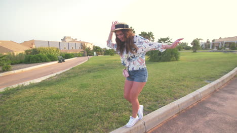 a young woman in a hat and floral shirt smiles as she walks along a path in a garden.