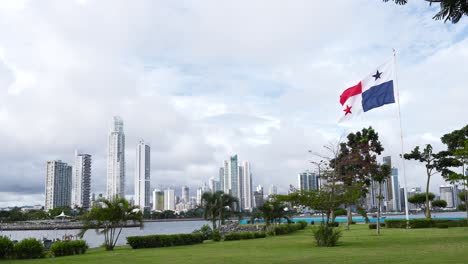 the national flag of panama gently waving the wind against a backdrop of modern tall buildings and skyscrapers near the coastline