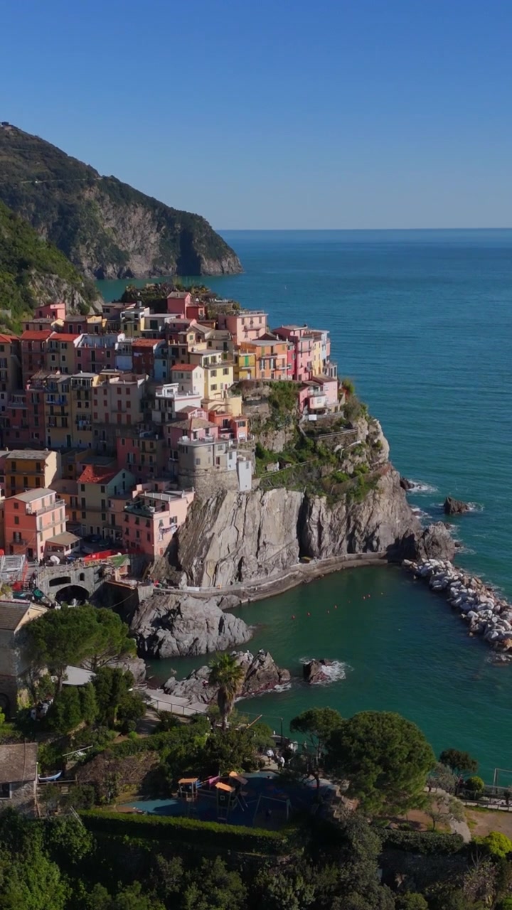 Vertikal dronestigning langs klippefyldte klipper for at afsløre landsbyen Manarola ovenfor.