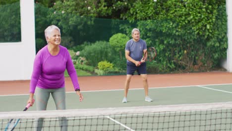 video de una feliz pareja de alto nivel biracial durante el entrenamiento en la cancha de tenis