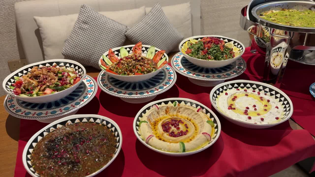 Färgglatt mellanöstern mezze-upplägg med hummus med olivolja, tabbouleh, färska hackade sallader och traditionella aptitretare arrangerade på ett matbord inomhus för en festlig måltid
