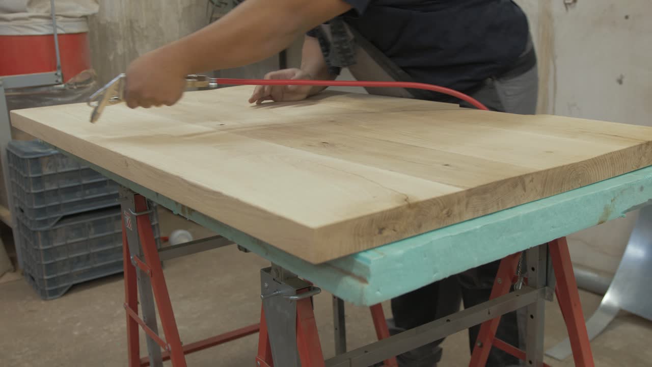 Blowing sawdust particles off oak tabletop prepared for varnish