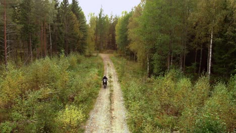 motorcyclist driving towards the camera on a small gravel road in the forest