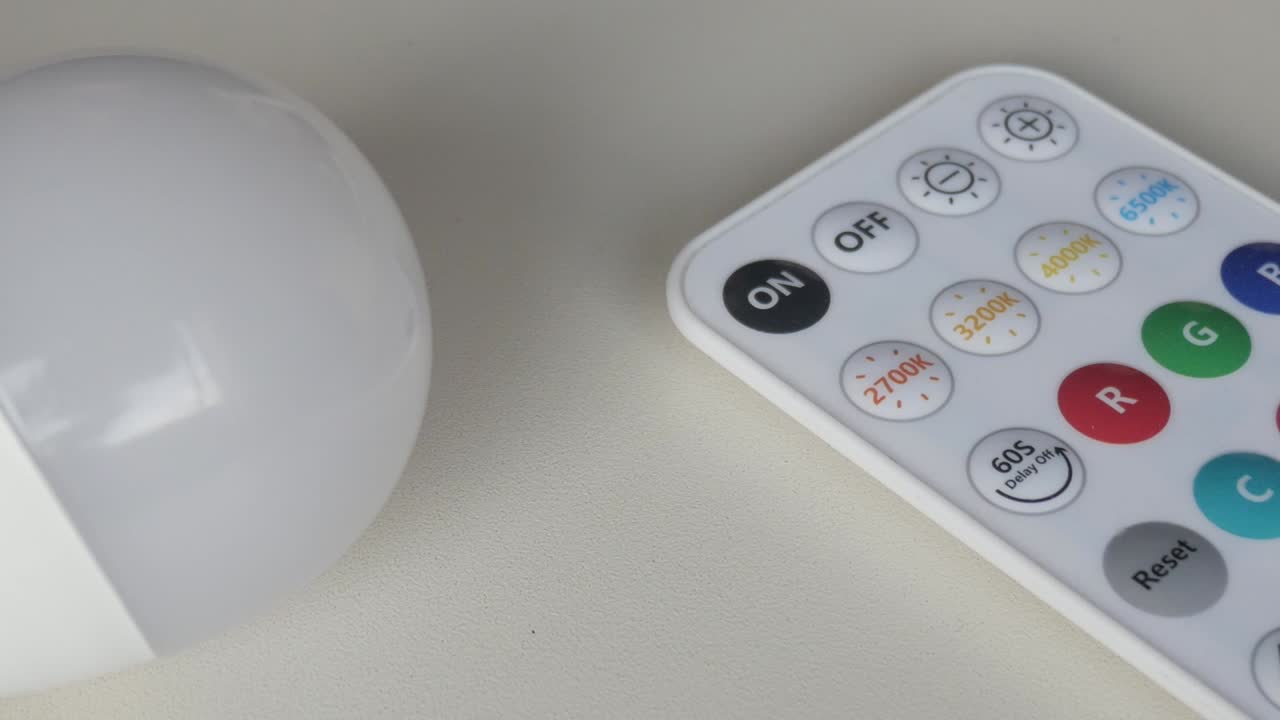 Lampadina LED intelligente e telecomando posizionati su superficie bianca, zoom indietro