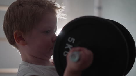 focused blond toddler pumps arm muscles with heavy barbell