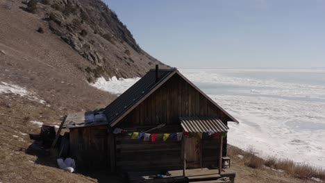 a drone hovers over a house with sacred tibetan flags on the rocky shore of lake baikal in winter.