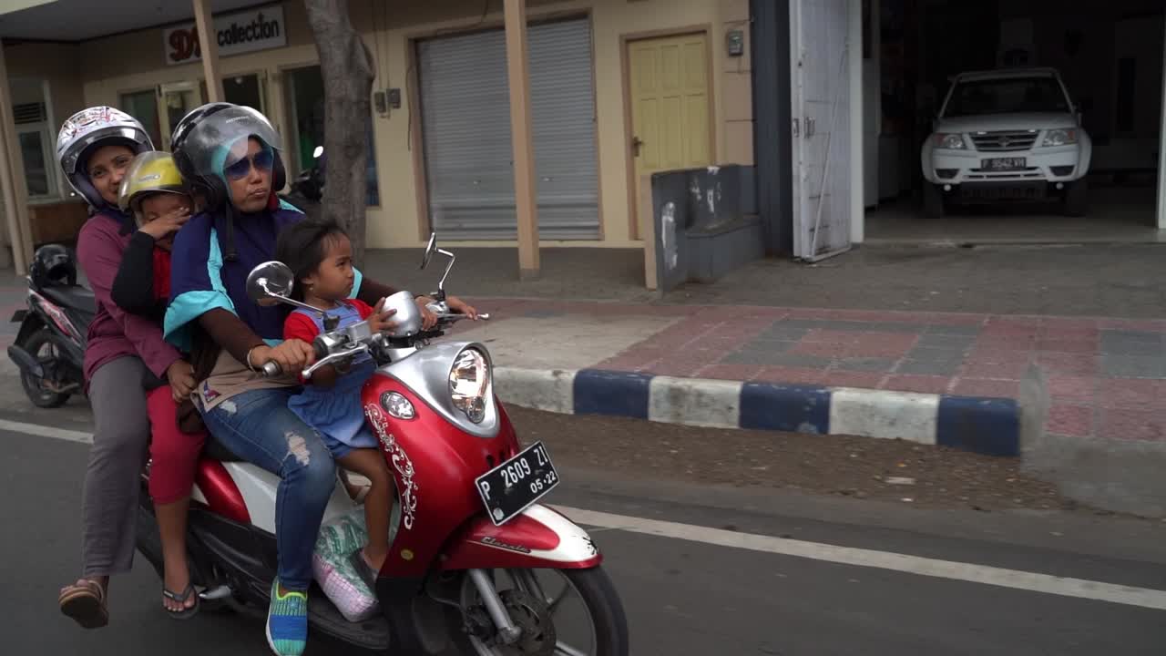A slow motion shot of a Javanese mother driving her child and and two others down the street on a scooter