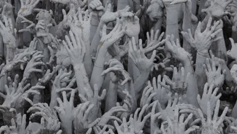 outstretched sculpted hands at the white temple in chiang rai, thailand, with visible feet moving on the bridge above the intricate design