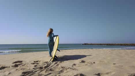 young girl wearing wetsuit and picking up surfboard on beach, getting ready for surfing