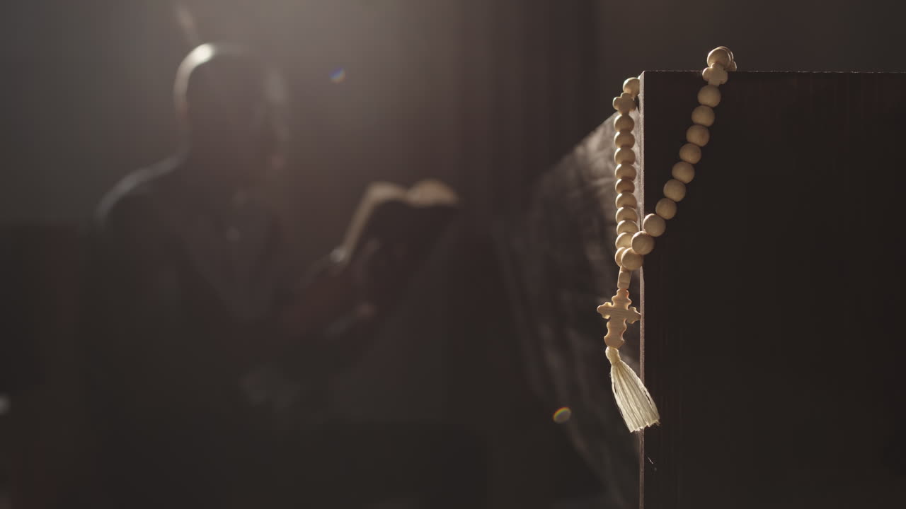 Rosary Beads and African-American Clergyman Reading Bible on Background