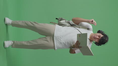 cuerpo lleno de hombre asiático estudiante sosteniendo libro y escuchando música con auriculares, bailando en el estudio de pantalla verde