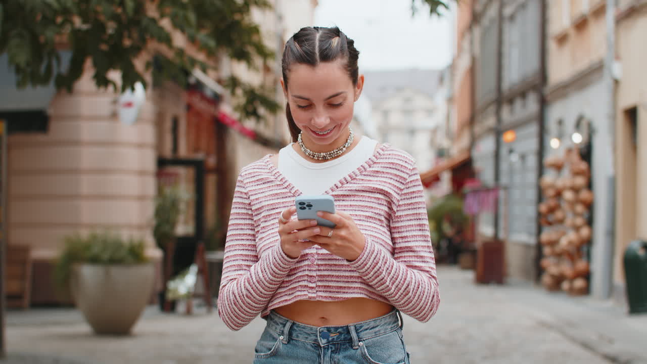 Giovane donna caucasica che usa lo smartphone, scrive messaggi sui social media, invia e-mail in una strada della città.
