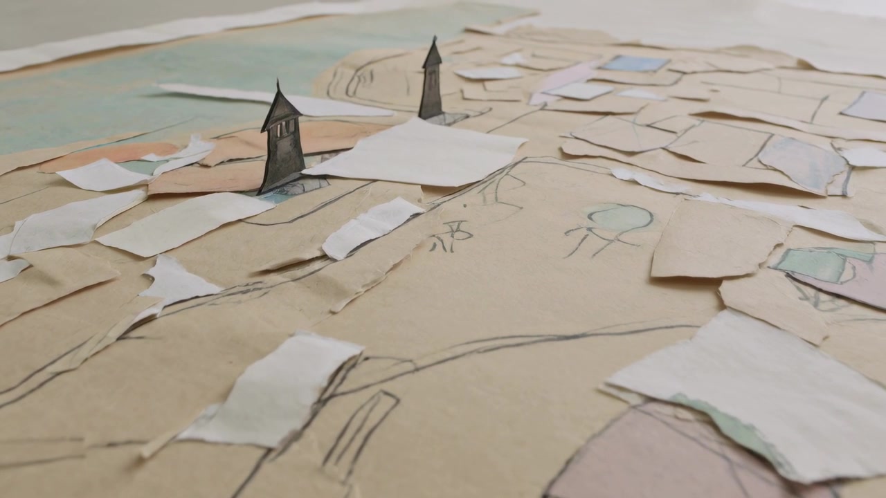 Panning low-angle camera revealing paper town on tan tabletop, highlighting torn rooftops
