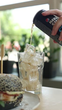 pouring soda into a glass with ice, alongside a burger