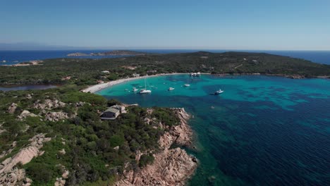 aerial sideways shot panoramic view of protected area of sardinia,italy with boats anchored off coast and people enjoying sun during holidays