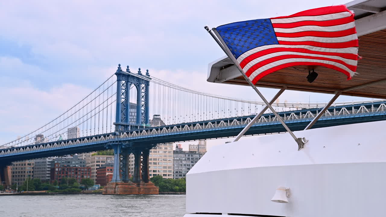 Una barca con una bandiera americana naviga sull'East River a New York. Il famoso Ponte di Manhattan sullo sfondo.