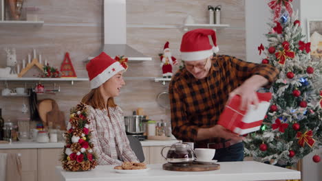 Abuelo-Nieta-Sorprendente-Con-Envoltorio-De-Regalo-En-Cocina-Decorada-De-Navidad