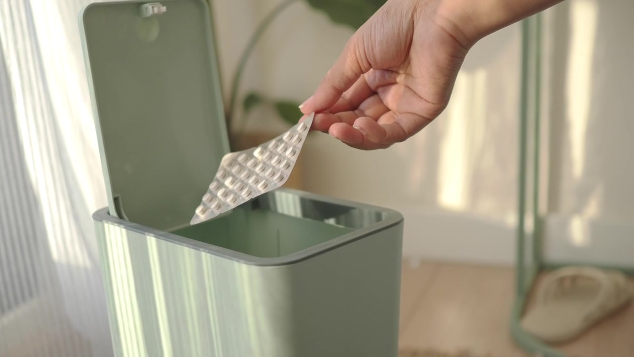 Hand Discarding Empty Pill Blister Pack into Trash Can