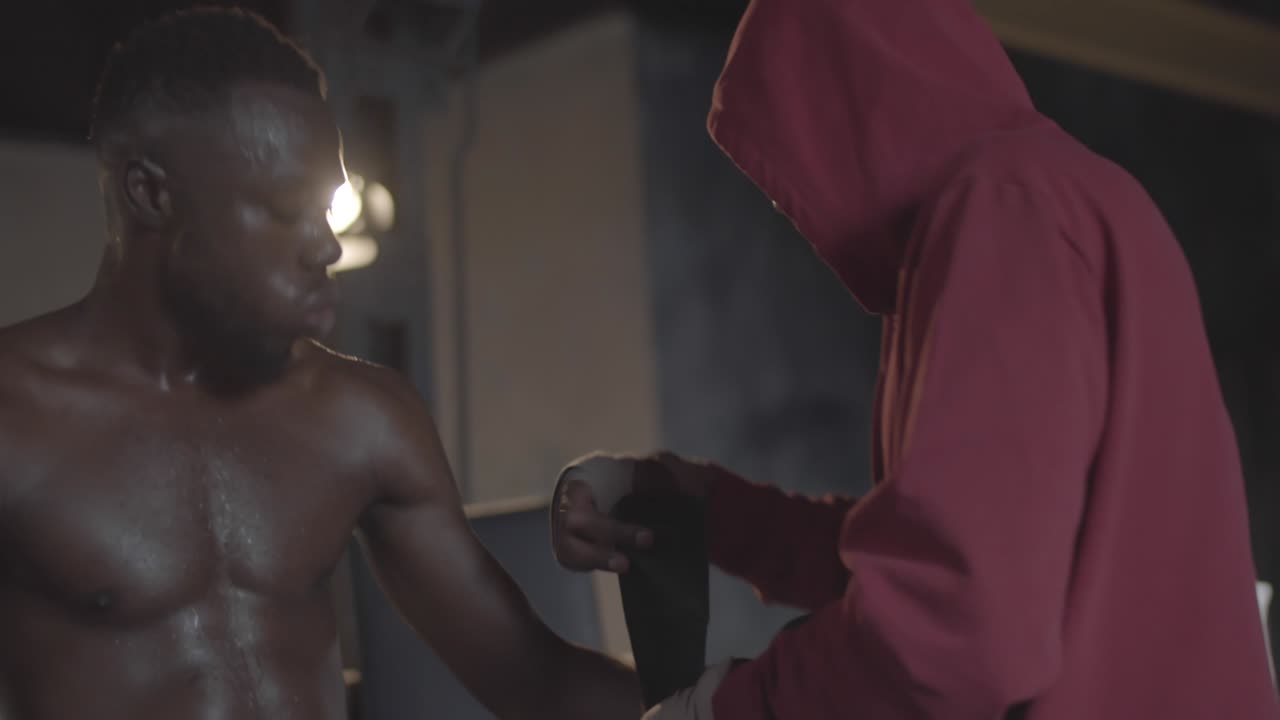 el entrenador se pone guantes para un boxeador negro sudoroso entre las rondas del partido.