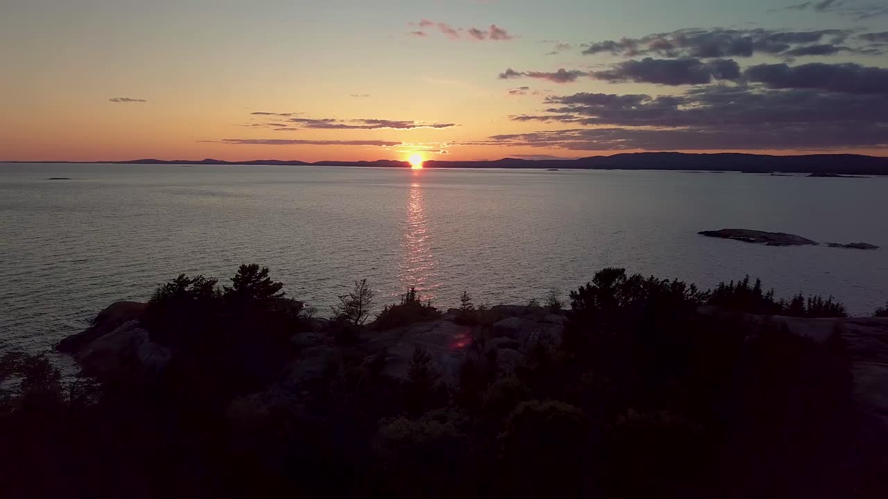Revelación de una isla rocosa con pinos en un lago azul al atardecer, alejamiento aéreo amplio con dron.