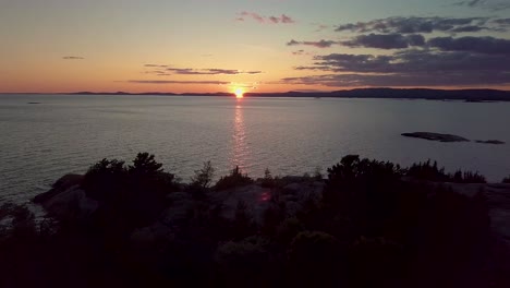 Reveal-of-Rocky-Pine-Tree-Island-in-Blue-Lake-at-Sunset,-Drone-Aerial-Wide-Dolly-Out