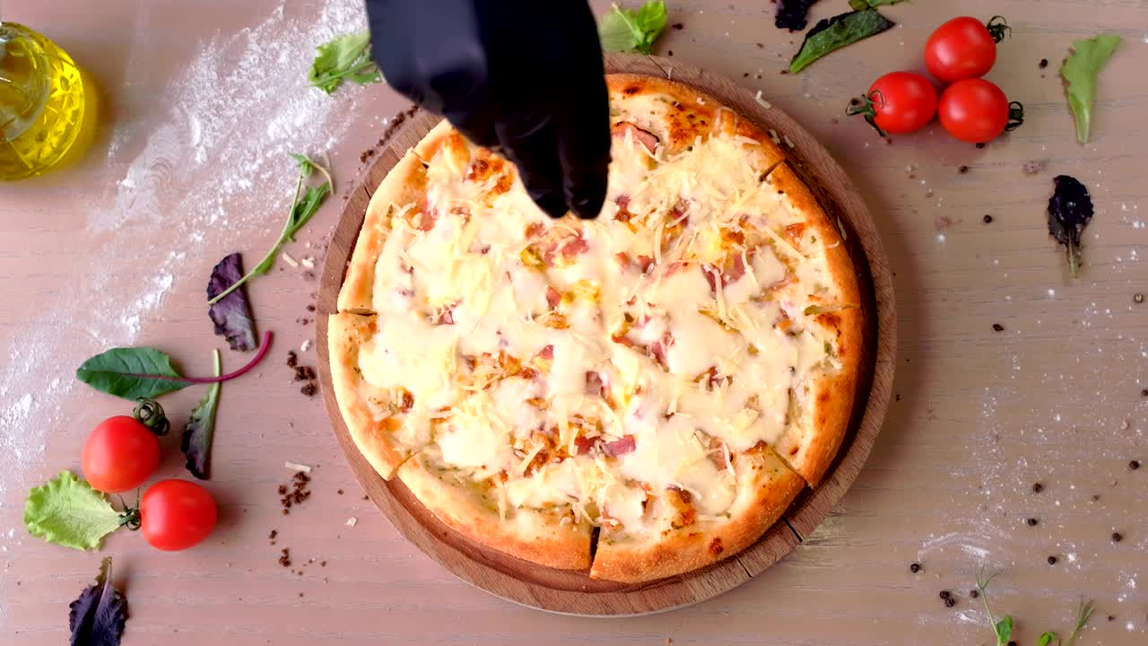 Chef sprinkle bacon pizza grated cheese. Hands in rubber gloves.