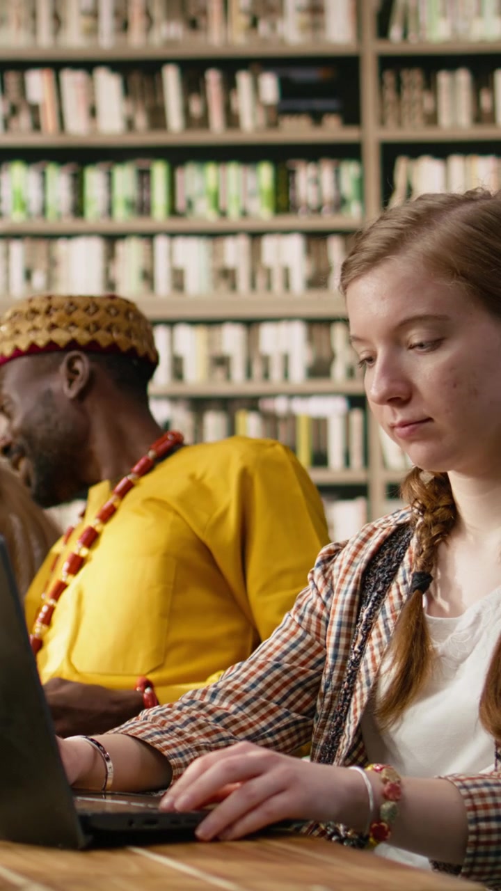 Video verticale: Giovane donna che prende appunti al laptop e studia accanto a un libro aperto.