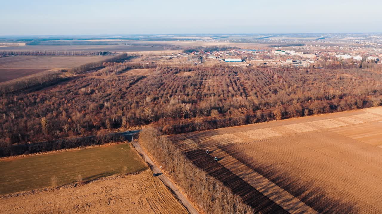 View of autumn farm fields, forest and road with cars. Aerial landscape of agriculture. Tractor cultivating land at sunset in field