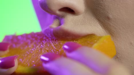 close up of woman's mouth eating juicy orange fruit against green background, studio shot