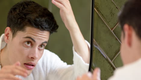 focused biracial man inspecting hair and face in bathroom mirror, slow motion