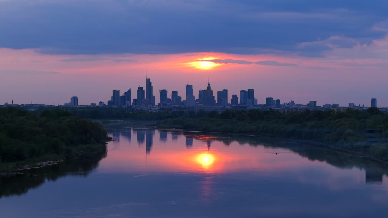 Vistula river with downtown district skyscrapers in background at sunset, Warsaw, drone shot